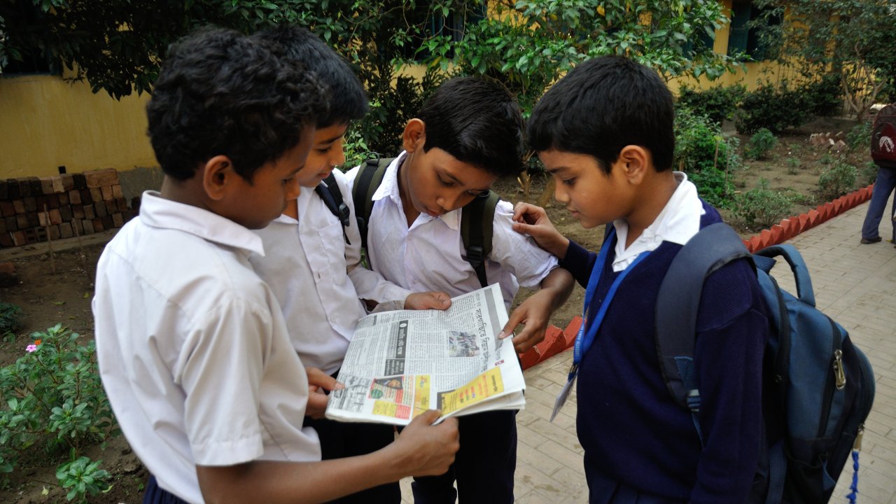 Students and community members reading newspaper updates and educational publications in India